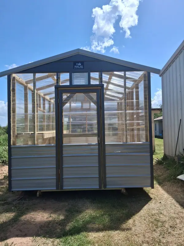 Front exterior of the 8x12 greenhouse with a single entry door and clear wall panels