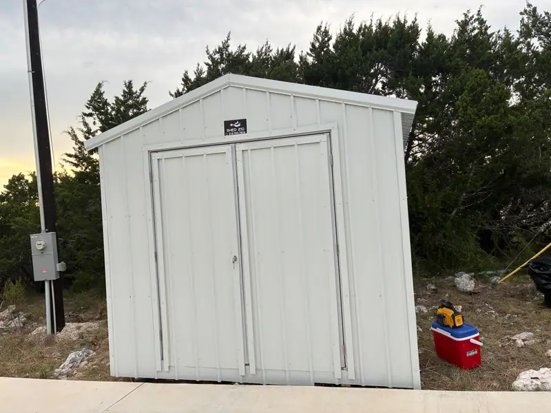 Straight-on view of the white 10x12 storage shed with vertical metal panels and wide double doors.