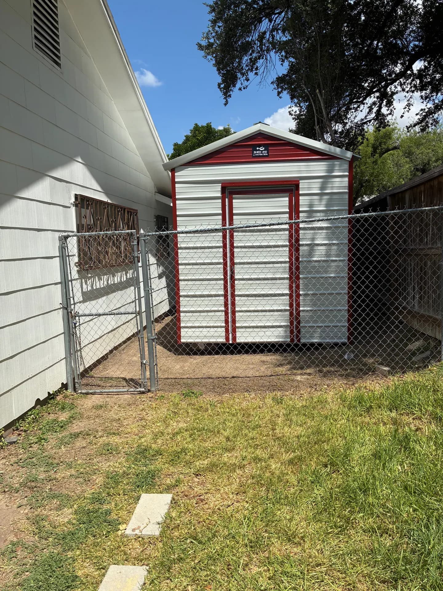 Front view of the finished 8x16x9 utility shed with light metal siding, red trim, and a single door in San Antonio, TX.