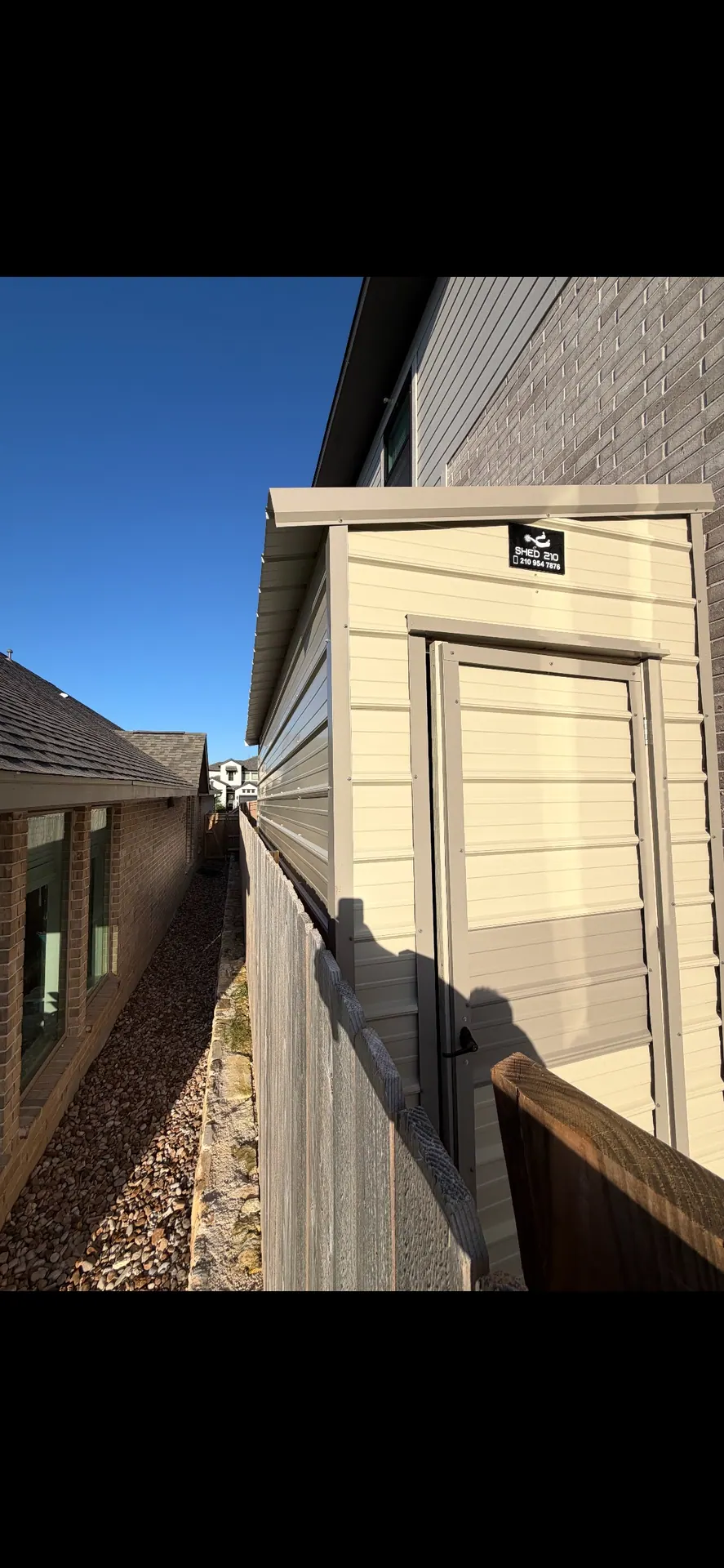 Angled view showing the entry door and long metal side of the narrow 6x16 shed beside a Bulverde home