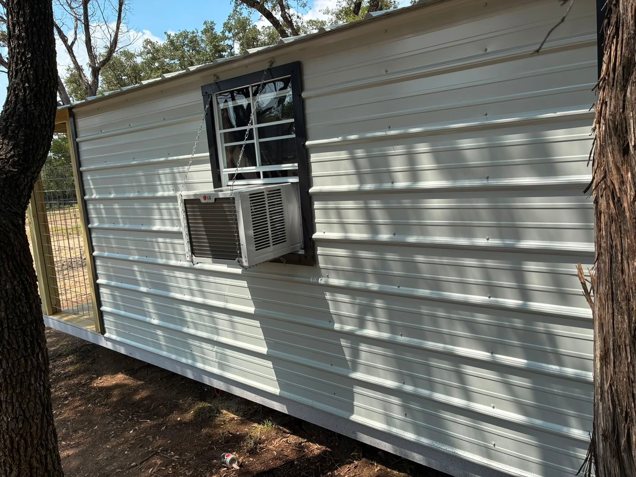 Side exterior of the cooled walk-in doghouse showing the window air conditioner