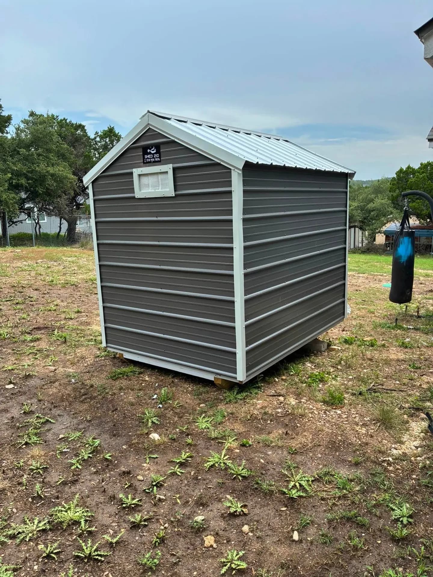 Back view of charcoal a-frame metal shed showing gable vent and white metal roof, built on-site in Lakehills, TX