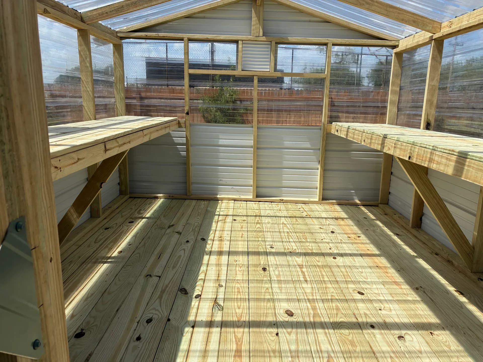 Wide greenhouse interior with two planting shelves, a wood floor, clear panels, and a rear ventilation louver.