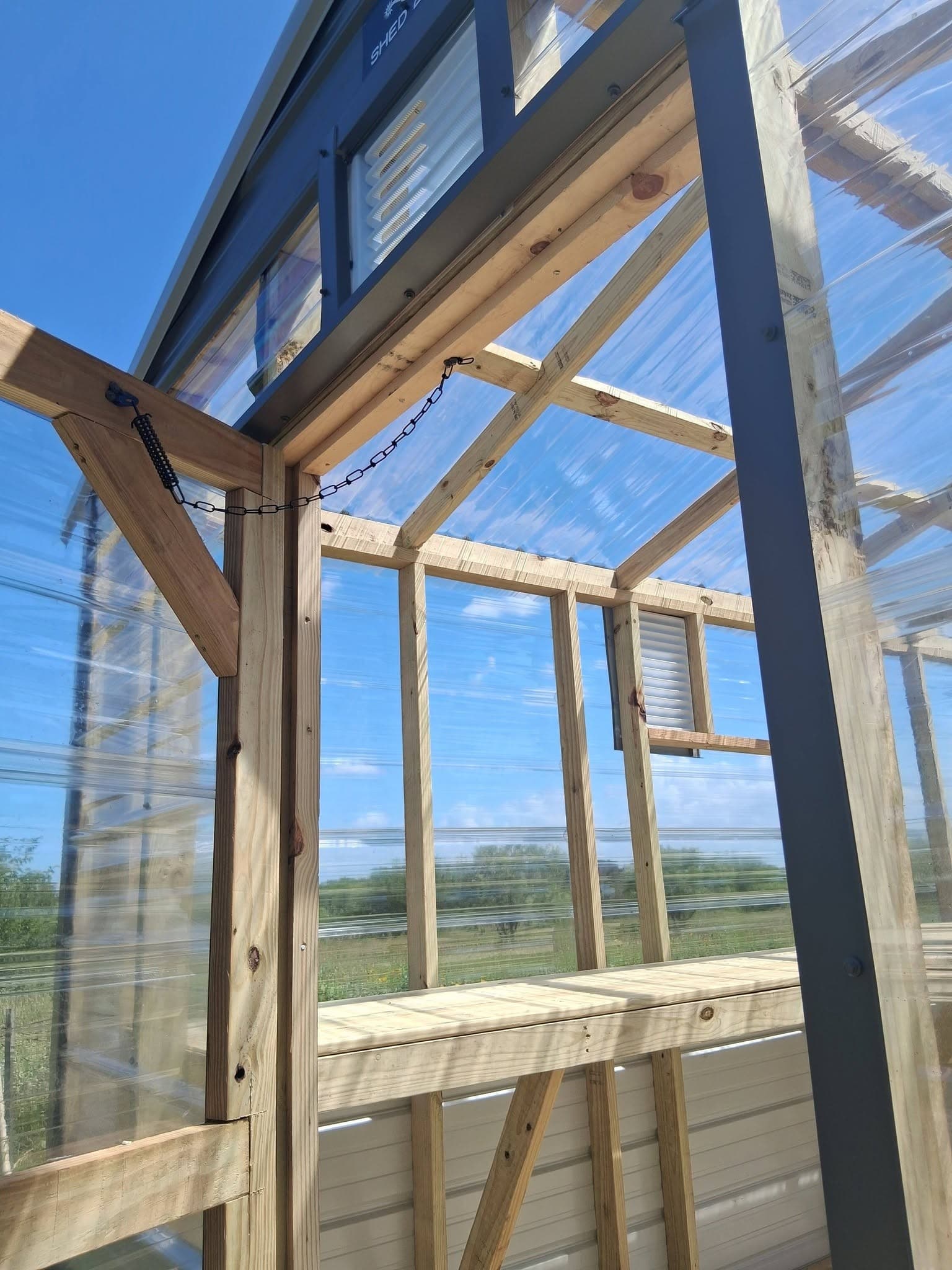 Interior detail showing the greenhouse entry door, clear roof panels, planting bench, and vent