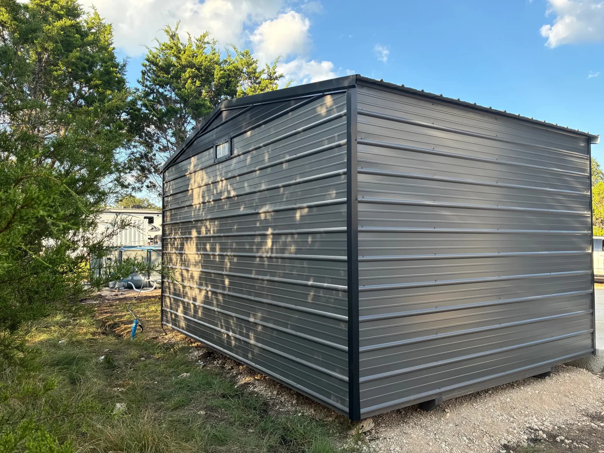 Rear and left-side view of the 12x16x9 utility shed with gray metal siding and black corner trim