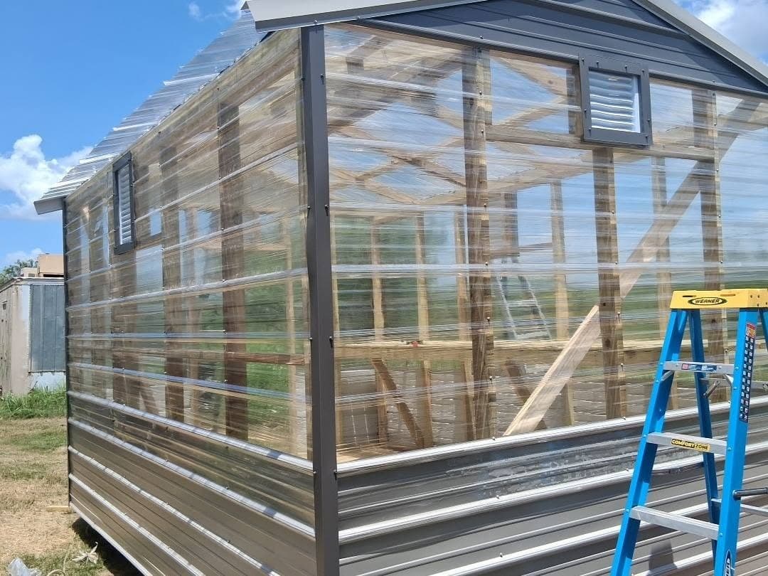 Side and rear exterior of the greenhouse showing clear panels, metal lower walls, and multiple vents