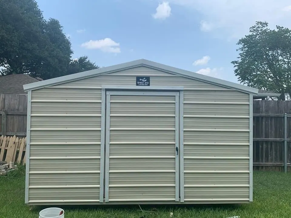 Straight-on view of the completed 8x12x7 Side Utility shed with Light Stone metal siding, white trim, and a closed entry door in Poteet.