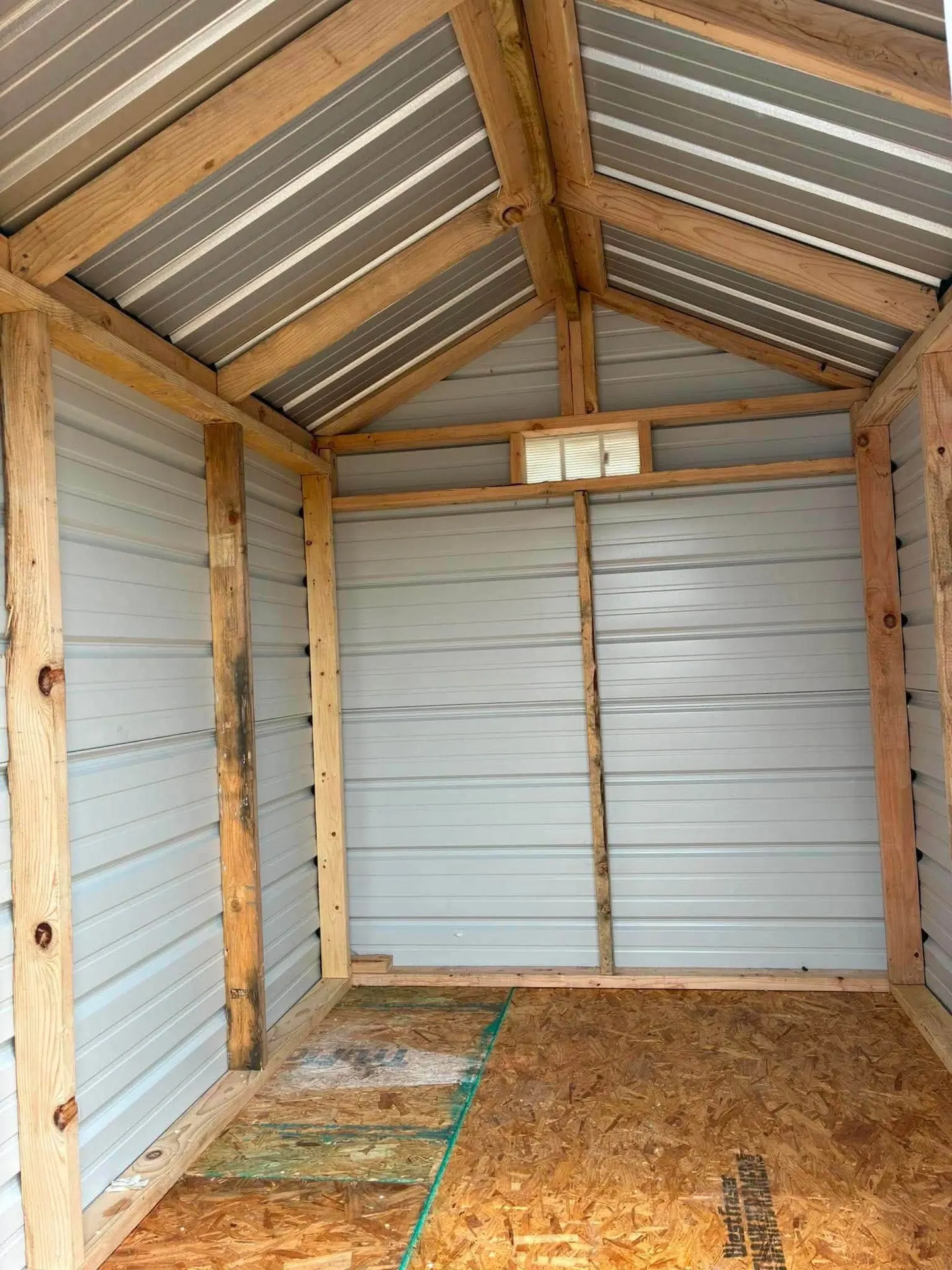 Interior of custom metal shed showing treated lumber framing, OSB floor, and gable vent