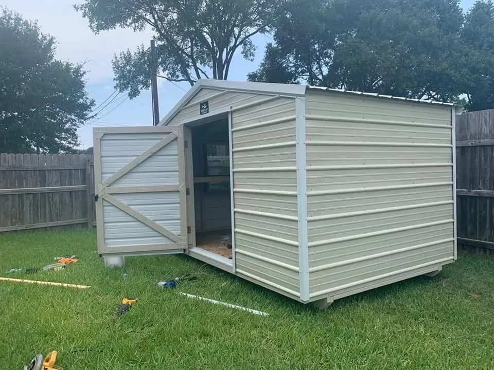 Three-quarter front view of the completed utility shed with its entry door open and Light Stone side wall visible.