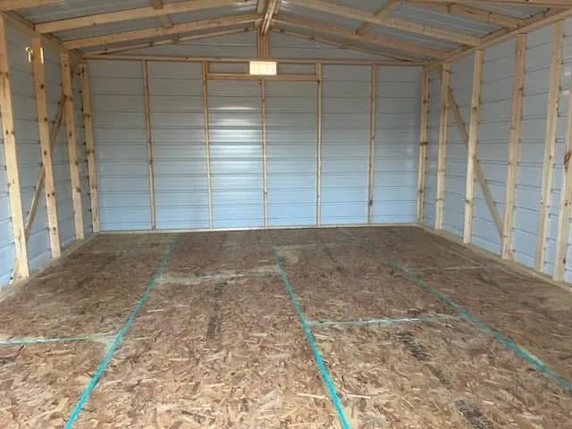 Open interior of the 16x20 shed showing exposed wood wall and roof framing above the wood-panel floor.
