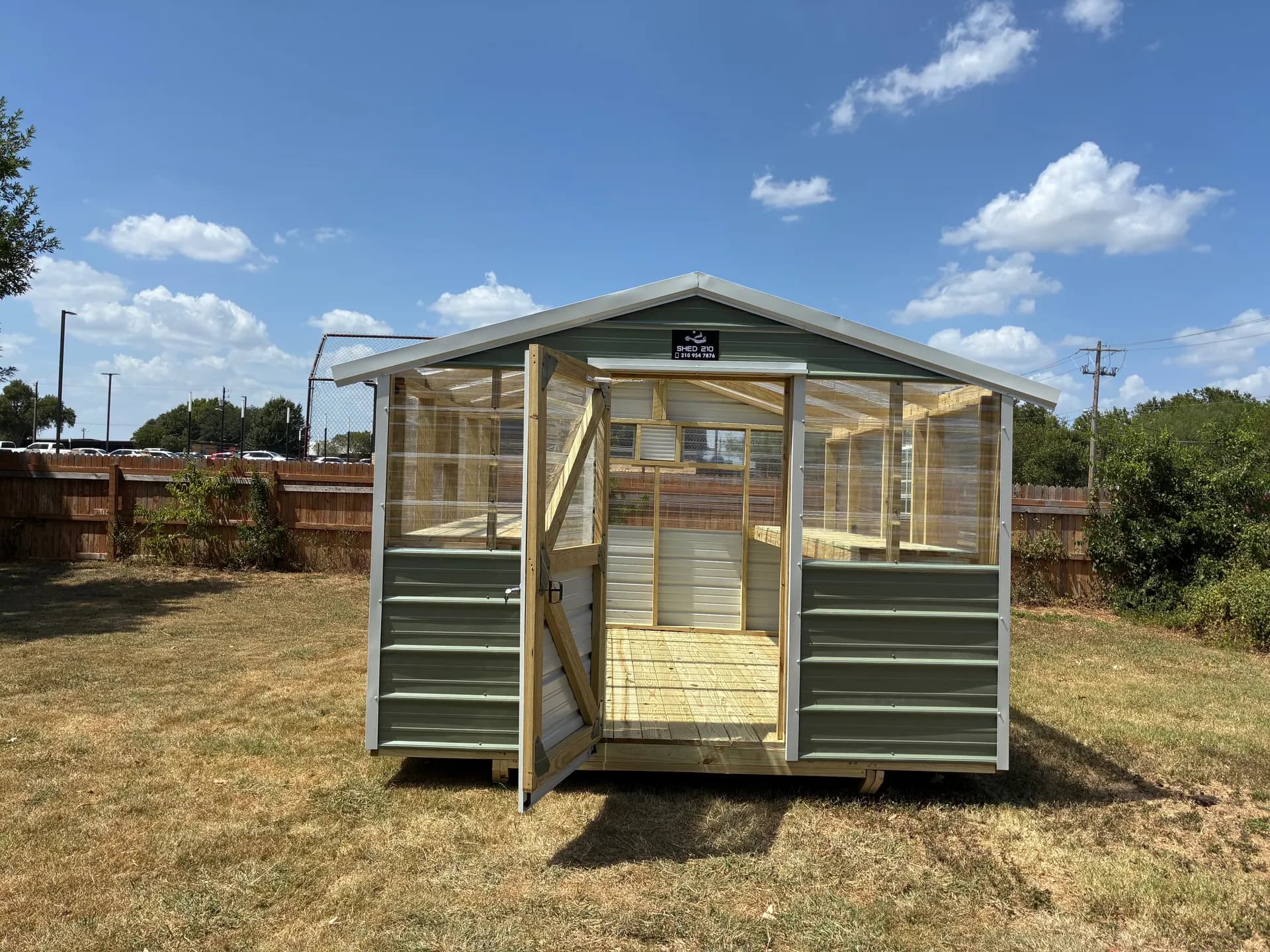 Front view of the completed 10x12 Luling greenhouse with its wood-framed walk-in door open.