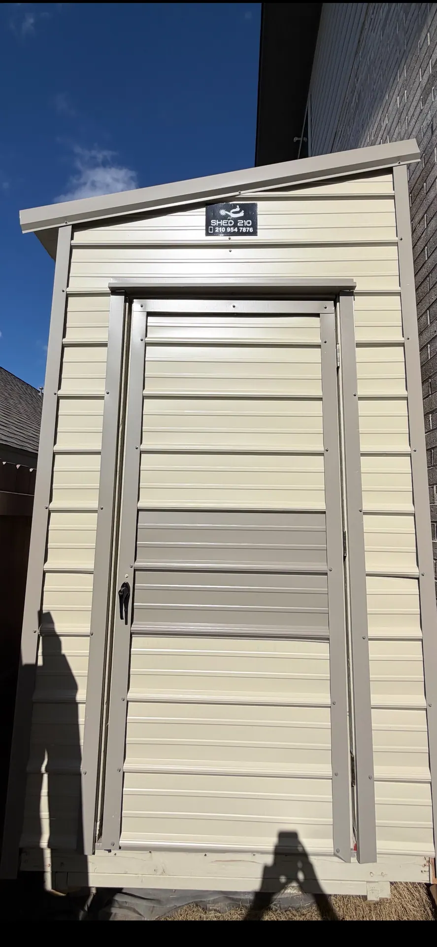 Close front view of the cream 6x16x9 Side Utility shed with tan trim, entry door, and single-slope roof in Bulverde, TX